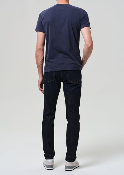 Man wearing a navy t-shirt and dark wash jeans against a grey background