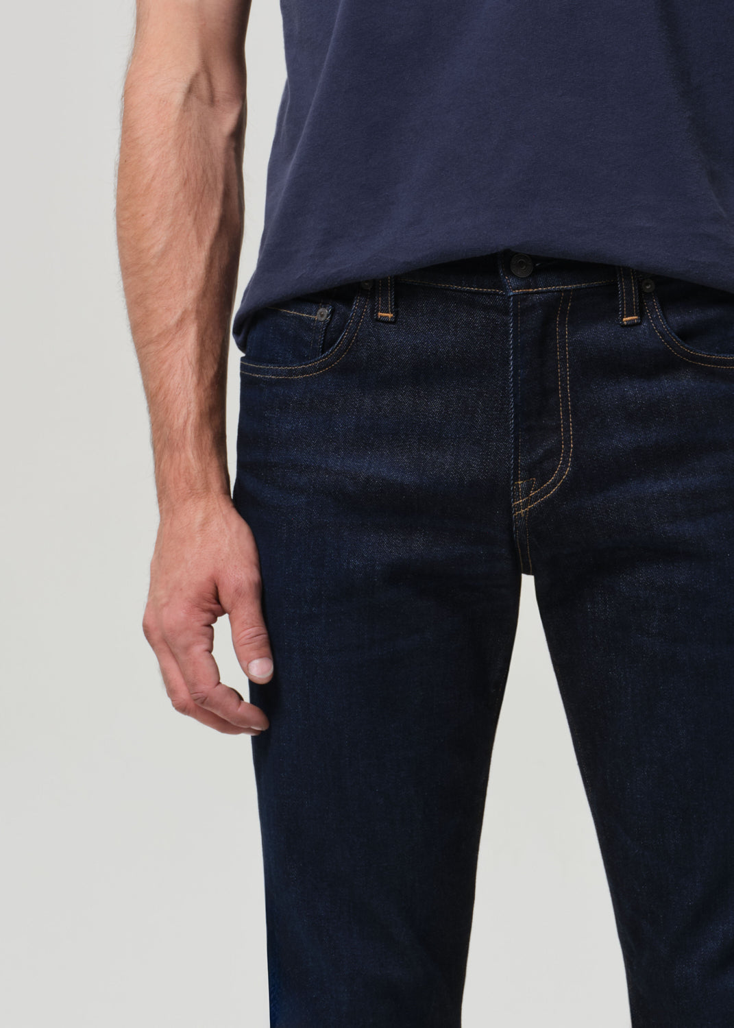 Man wearing a navy t-shirt and dark wash jeans against a grey background
