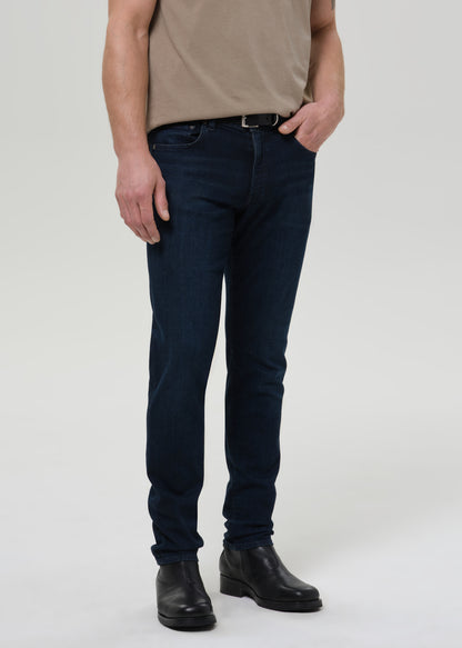 Person wearing dark blue jeans and a beige shirt on a grey background