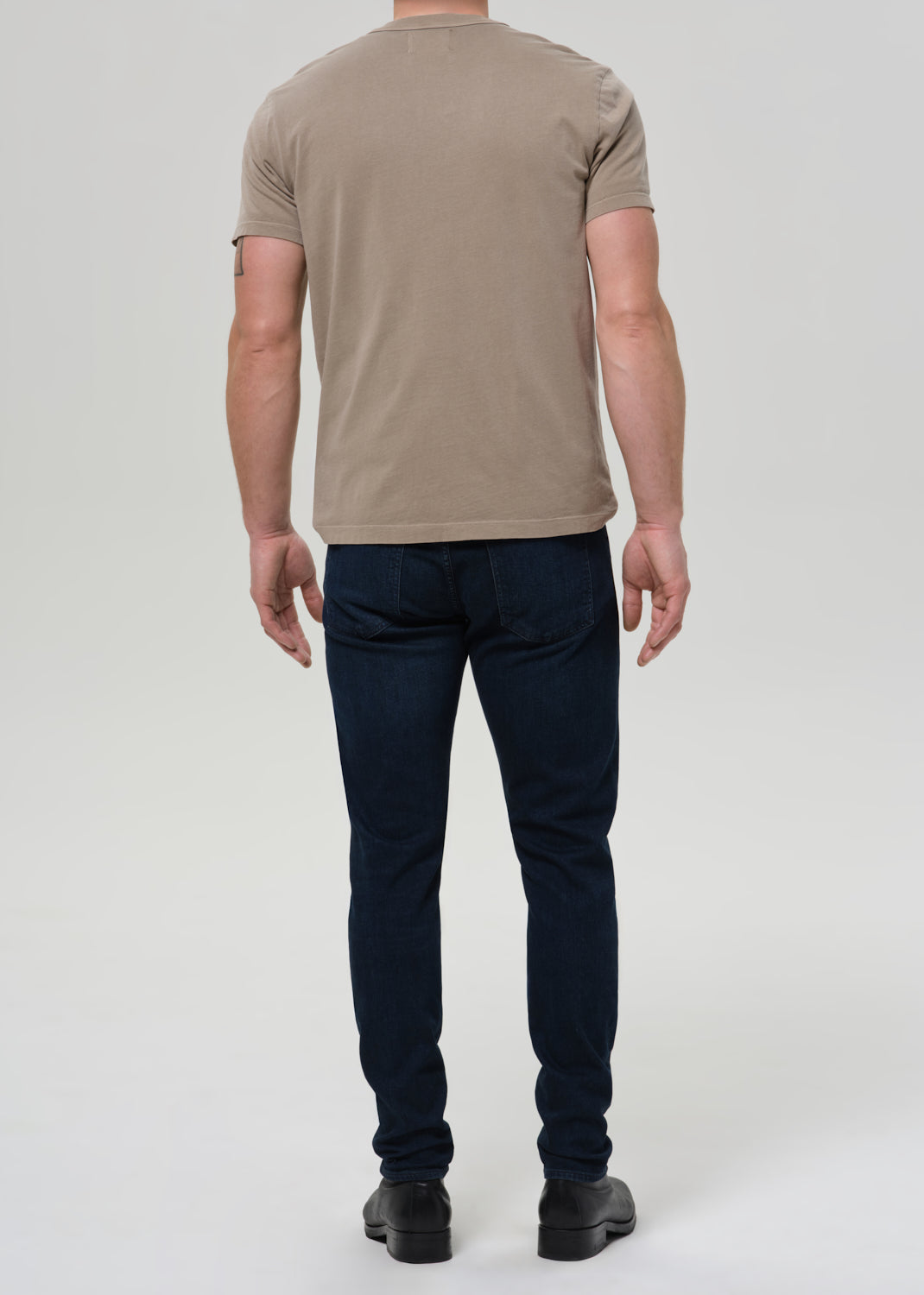 Person wearing a beige t-shirt and dark jeans on a white background
