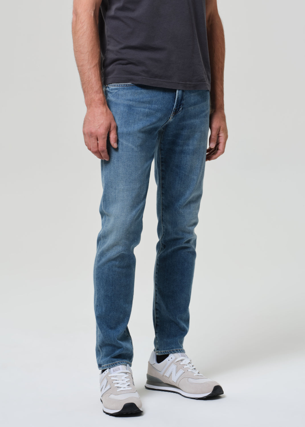 Person wearing blue jeans and white sneakers on a plain background