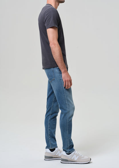 Person wearing a dark gray t-shirt and blue jeans on a light gray background