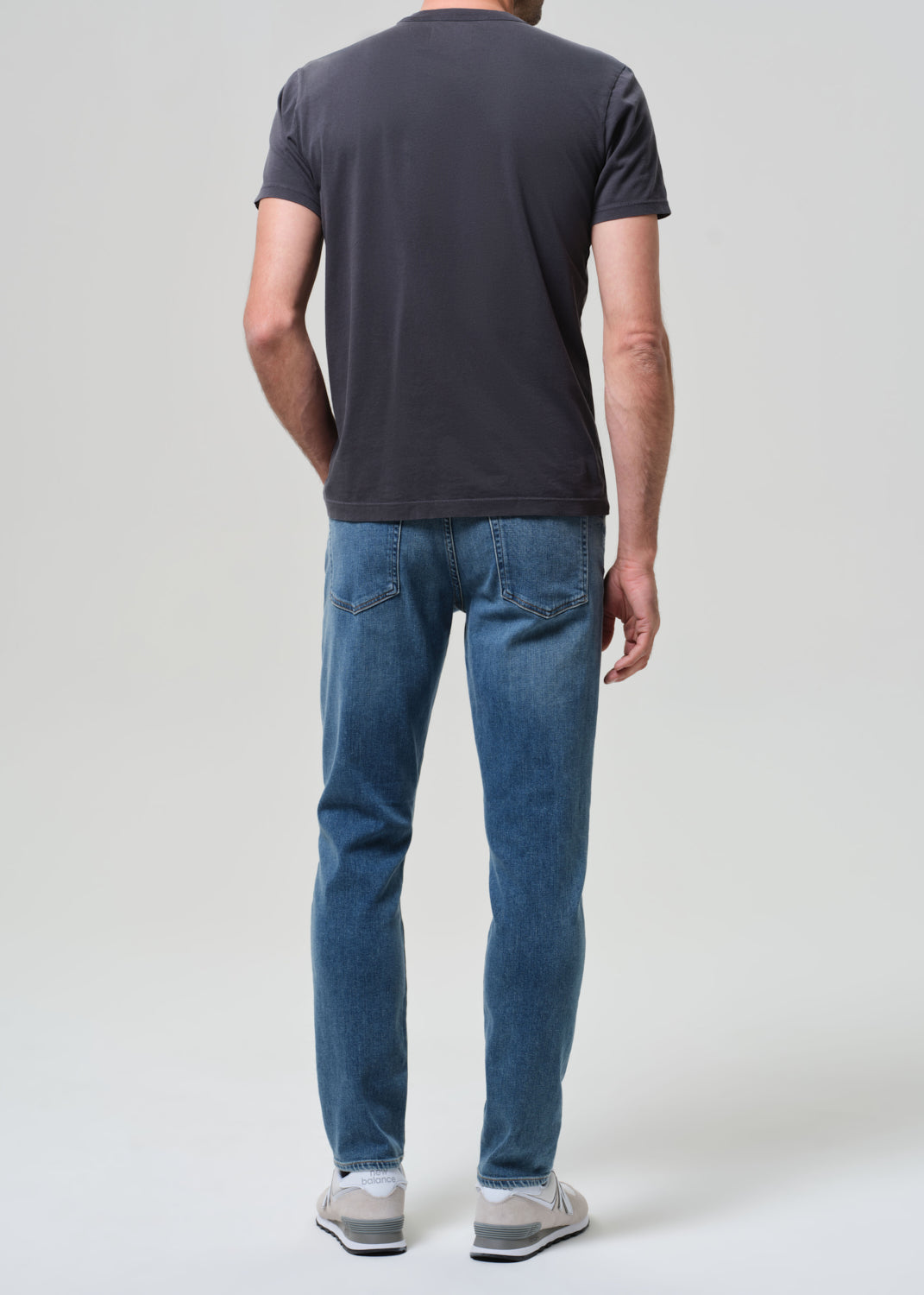 Person wearing a dark gray t-shirt and blue jeans on a white background