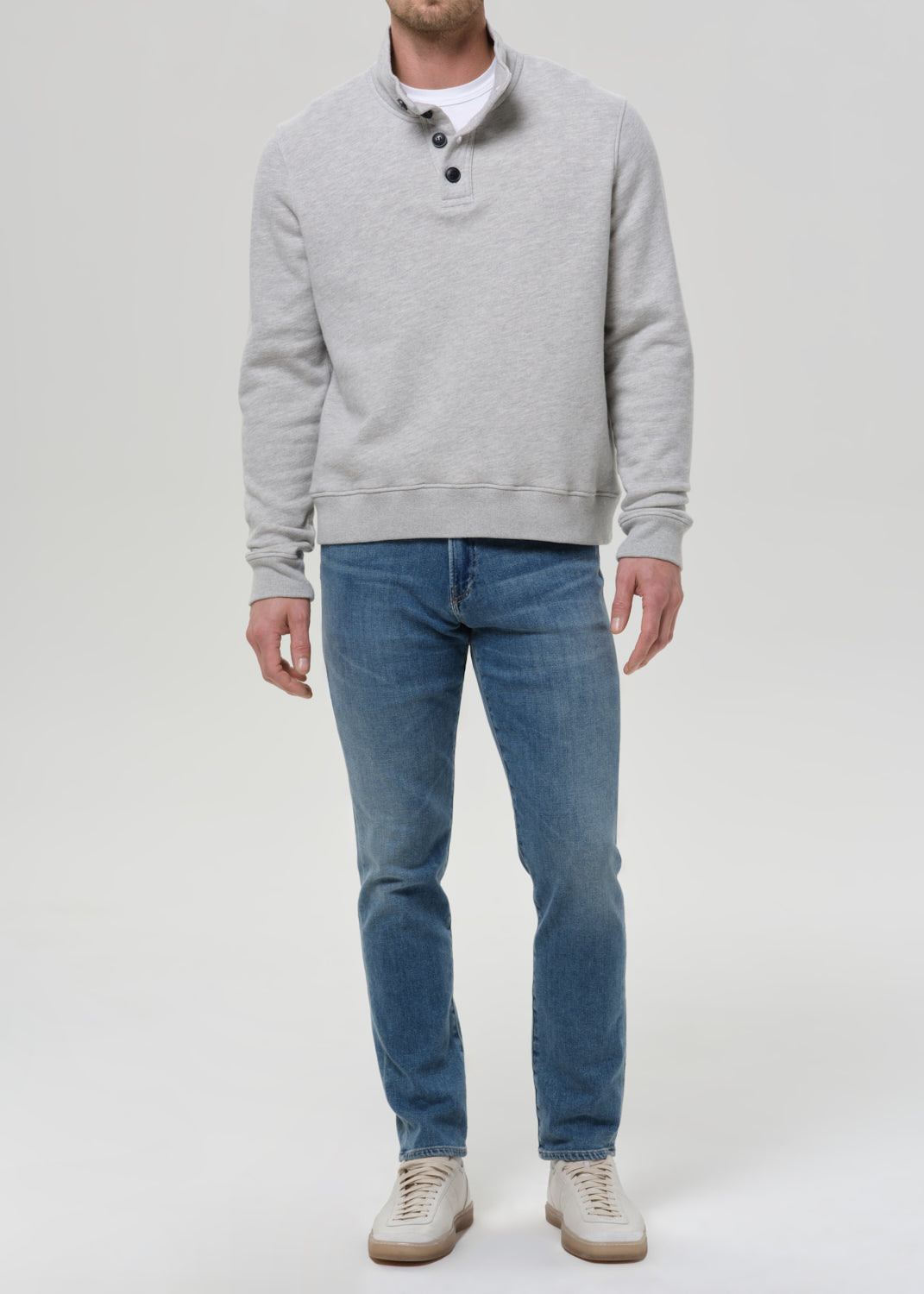Man wearing medium blue straight leg jeans with a light grey crewneck sweatshirt on a grey background.