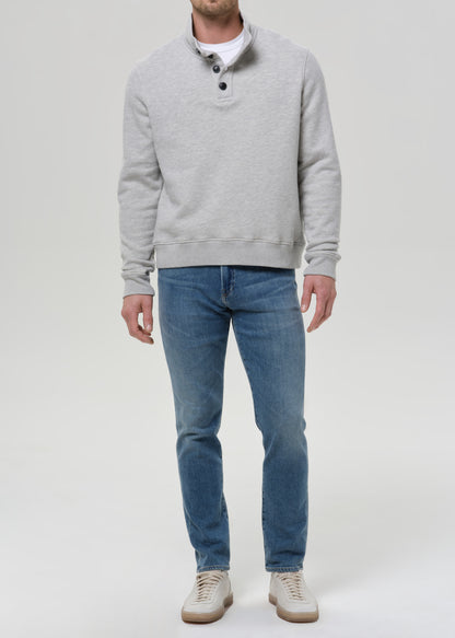 Man wearing medium blue straight leg jeans with a light grey crewneck sweatshirt on a grey background.