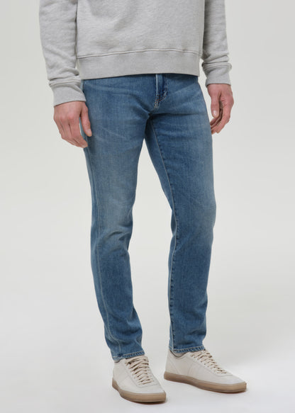 Man wearing medium blue straight leg jeans with a light grey crewneck sweatshirt on a grey background.