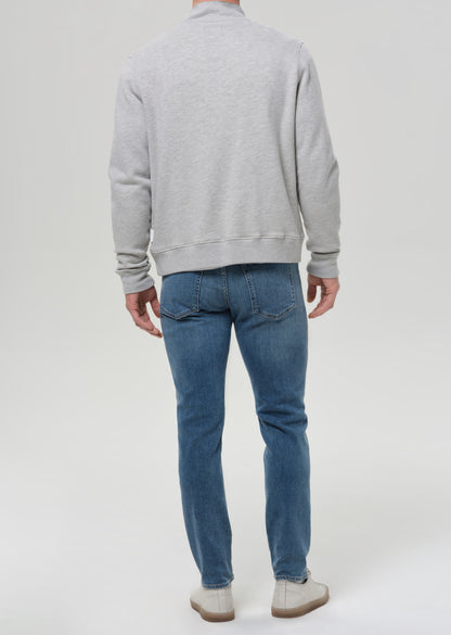 Man wearing medium blue straight leg jeans with a light grey crewneck sweatshirt viewed from the back on a grey background.