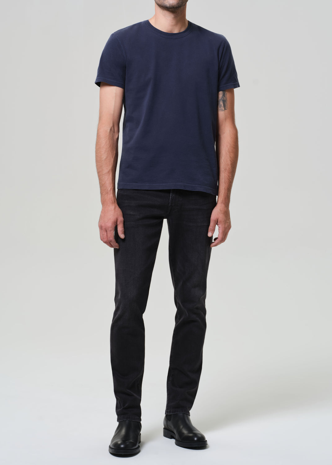 Person wearing a navy t-shirt and dark jeans on a grey  background