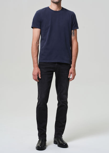 Person wearing a navy t-shirt and dark jeans on a grey  background