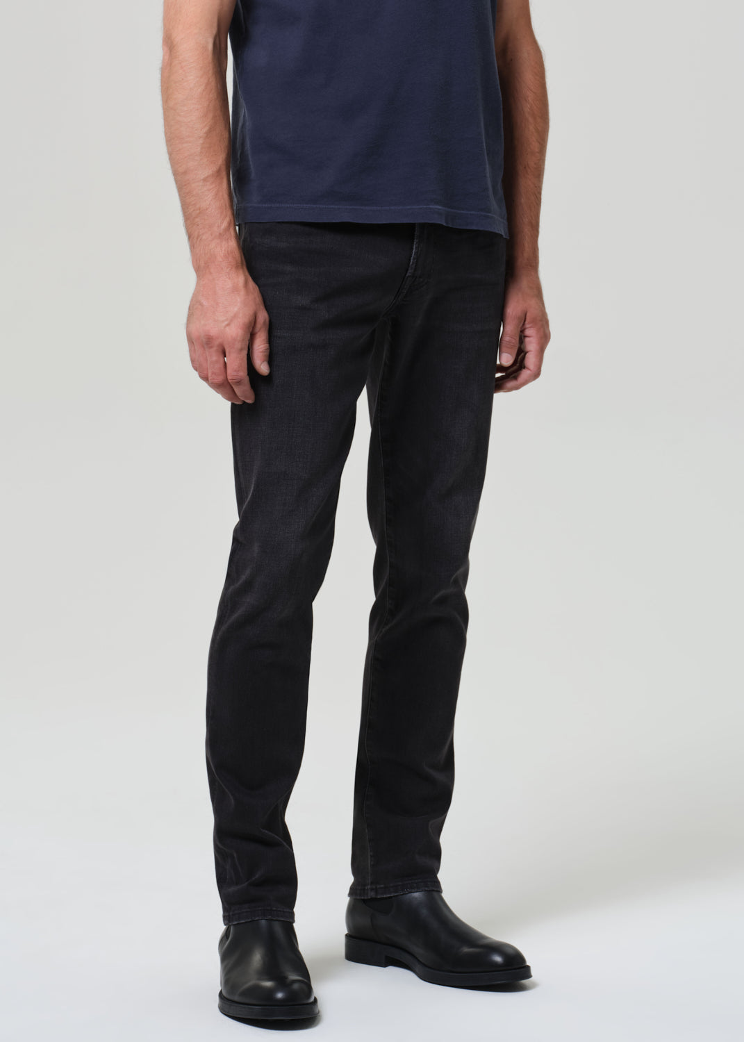 Person wearing a navy t-shirt and dark jeans on a grey  background