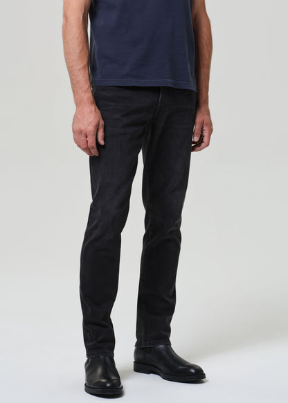 Person wearing a navy t-shirt and dark jeans on a grey  background