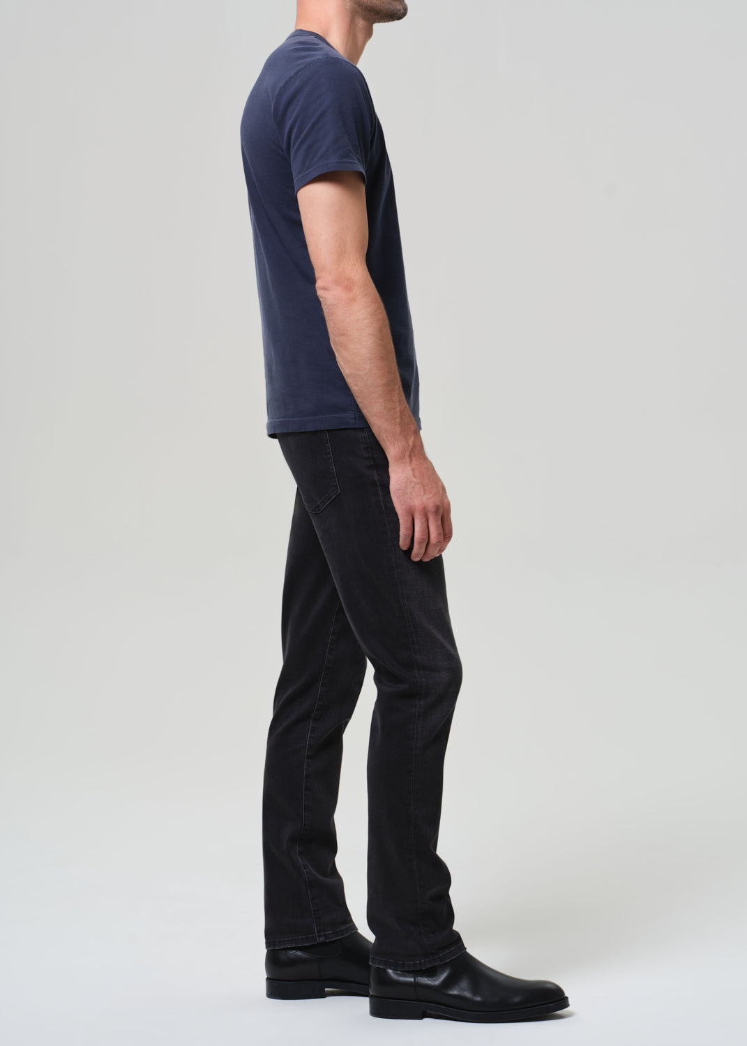 Person wearing a navy t-shirt and dark jeans on a grey  background