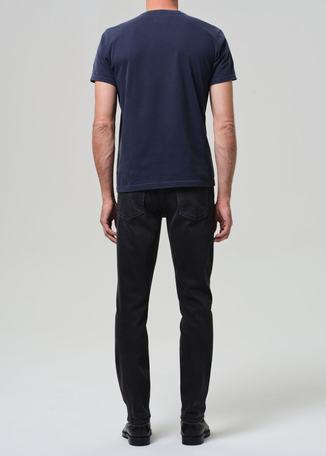 Person wearing a navy t-shirt and dark jeans on a grey  background