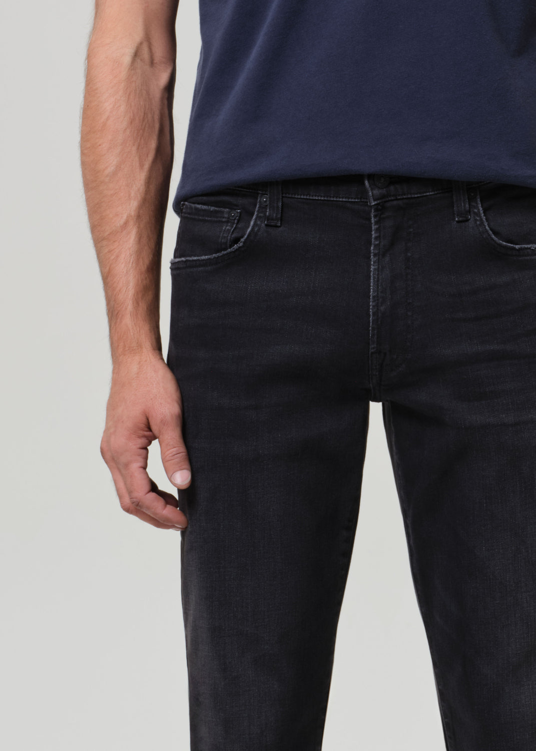 Person wearing a navy t-shirt and dark jeans on a grey  background