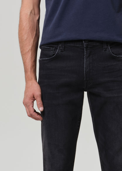 Person wearing a navy t-shirt and dark jeans on a grey  background