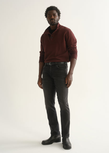 Person wearing a burgundy long sleeve polo shirt, washed black jeans, and black boots, angled front full body view on a light grey background.