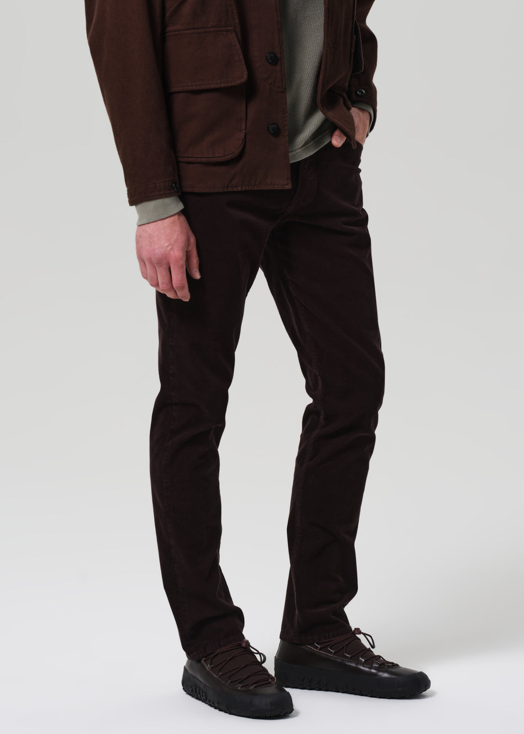 Person wearing dark brown pants and shoes on a plain background