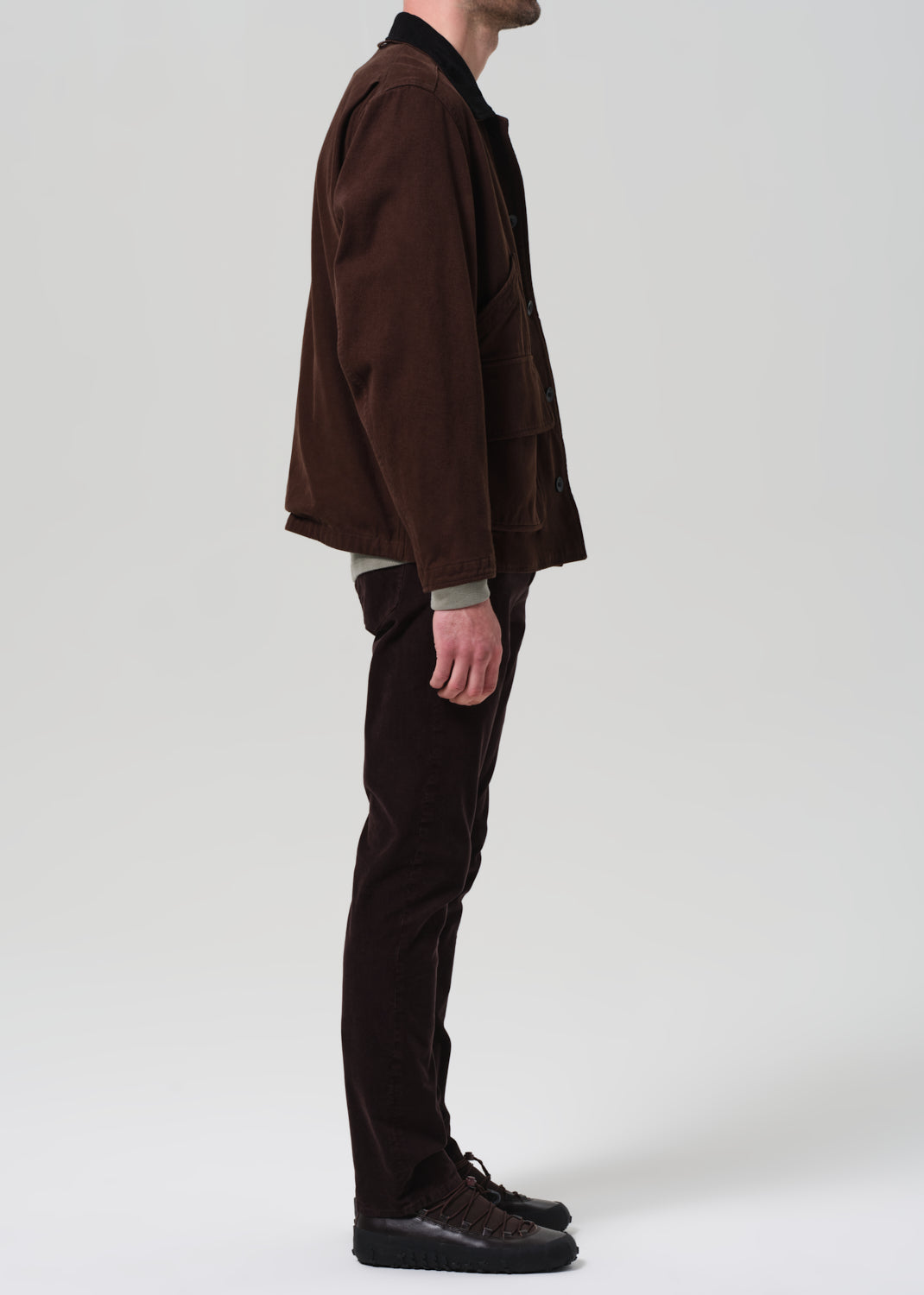 Person wearing a brown jacket and black pants on a plain background