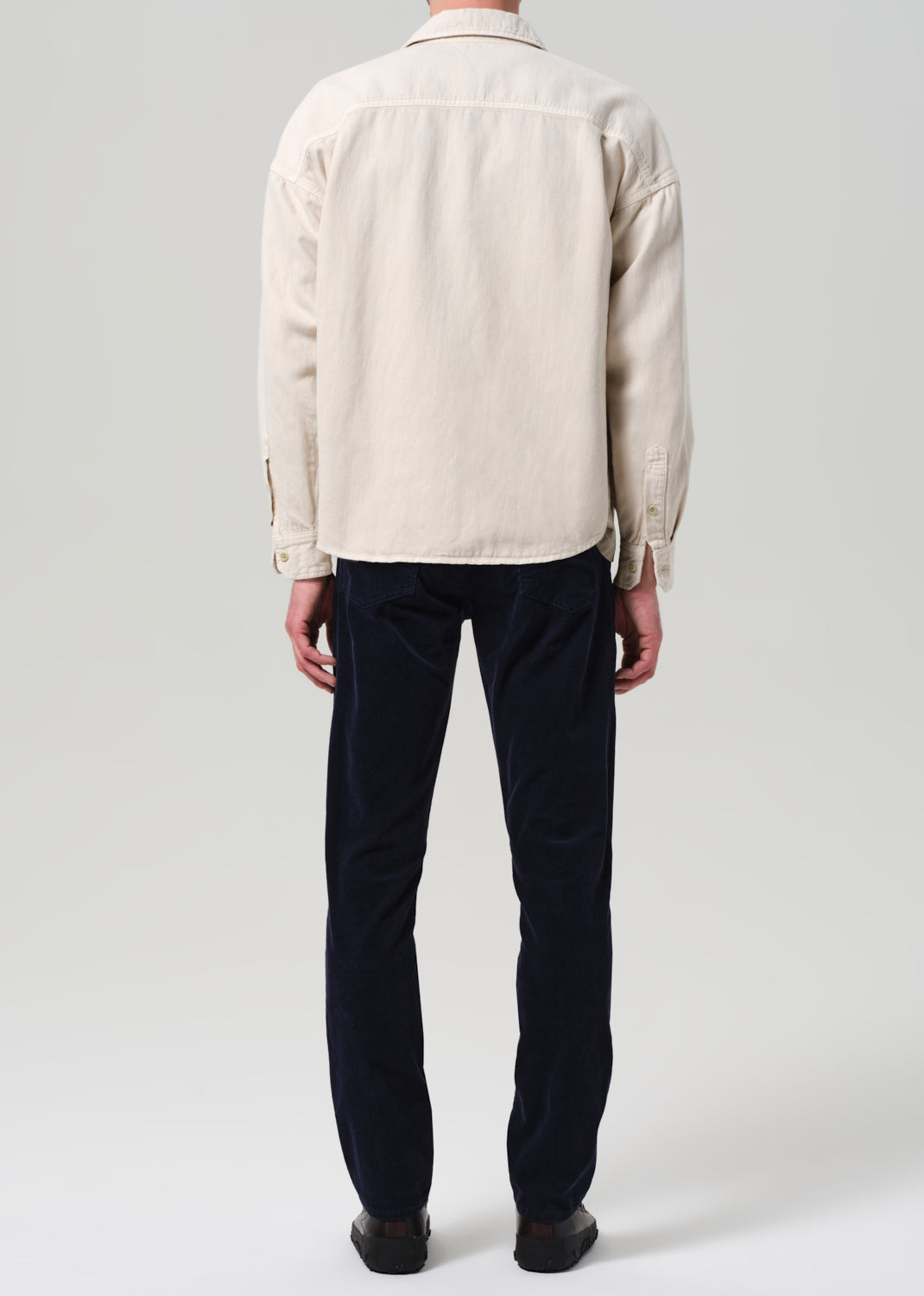 Person wearing a light-colored shirt and dark blue pants on a plain background