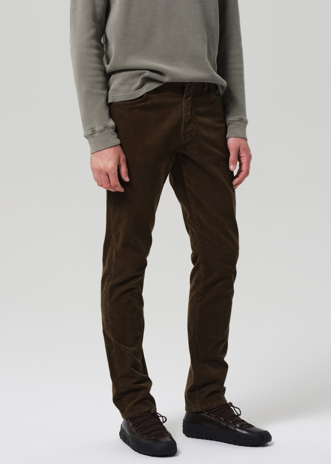 Person wearing a green sweater and brown pants on a plain background