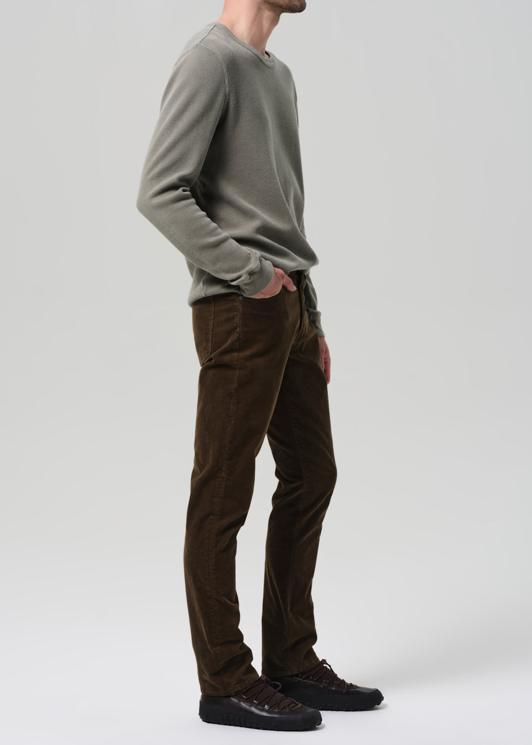 Person wearing a green sweater and brown pants on a plain background