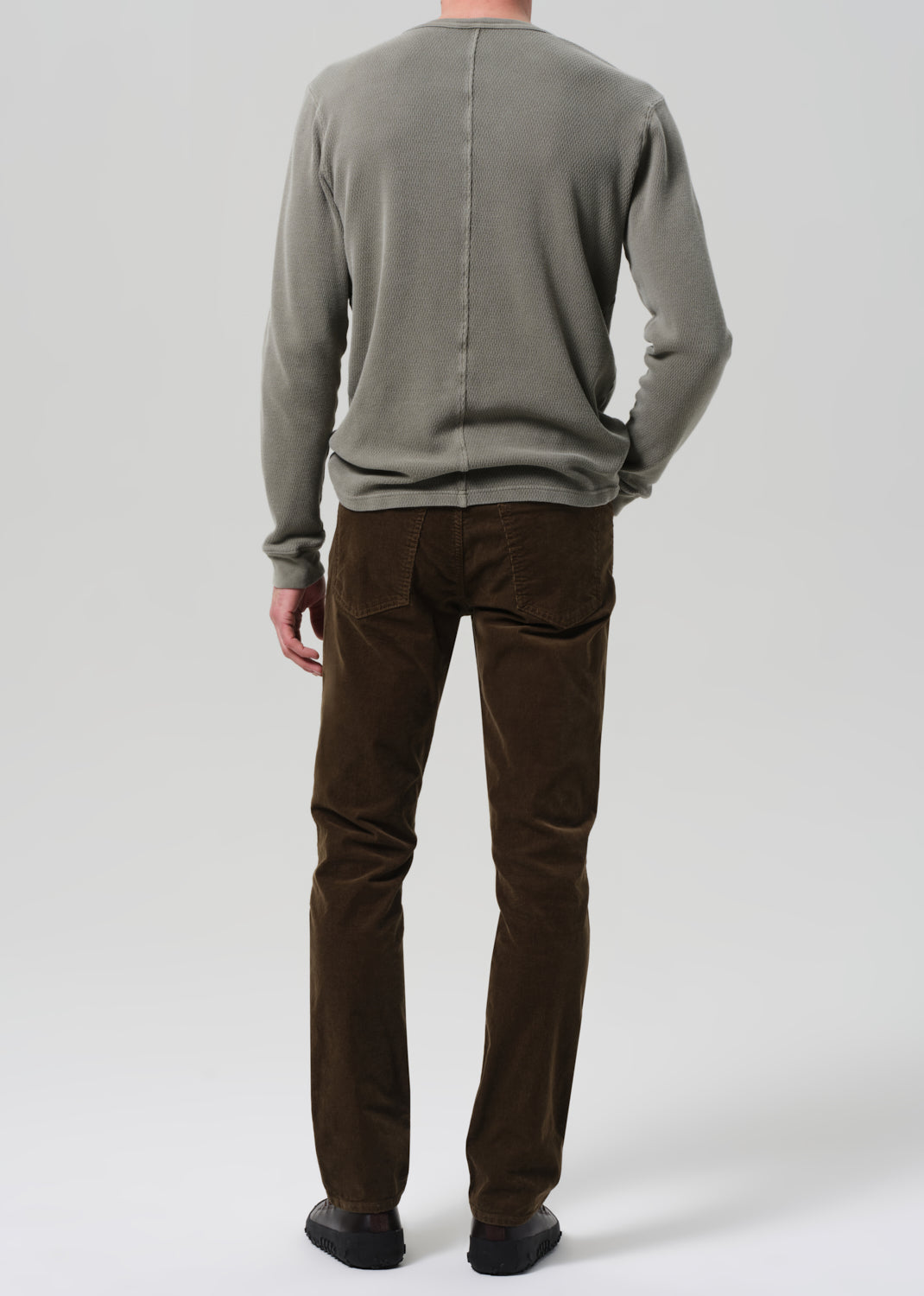 Person wearing a green sweater and brown pants on a plain background