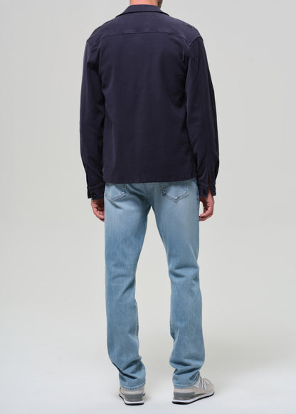 Person wearing a navy jacket, dark shirt, light blue jeans, and white sneakers on a plain background