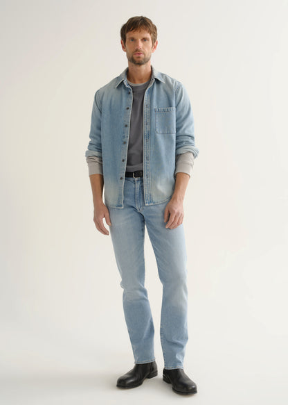 Person wearing a light blue denim shirt over a grey top, light wash blue jeans, and black shoes, front full body view on a light grey background.