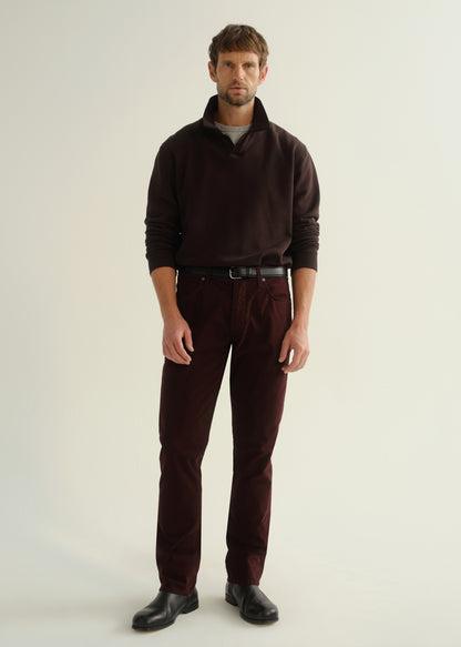 Person wearing a dark brown collared pullover sweatshirt, burgundy straight leg pants, and black leather boots, angled front full body view on a light grey background.