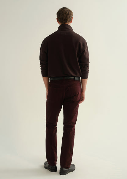 Person wearing a dark brown collared pullover sweatshirt, burgundy straight leg pants, and black leather boots, back full body view on a light grey background.
