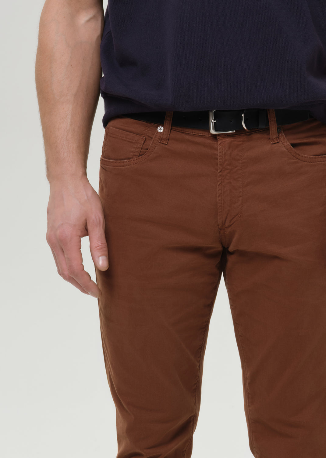 Close-up of brown straight leg pants on a grey background.
