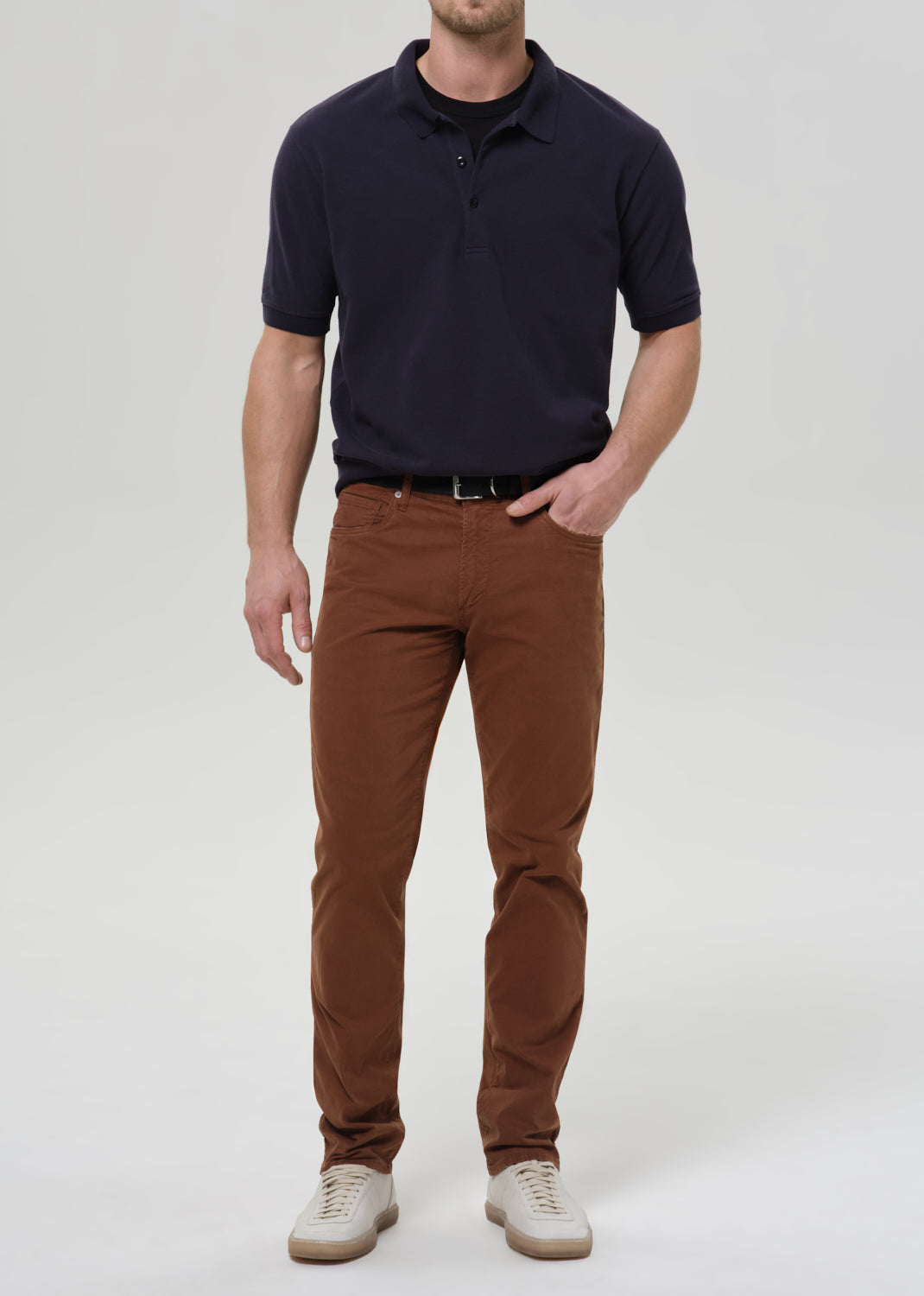Person wearing brown straight leg pants with a navy crewneck short sleeve tee on a grey background.