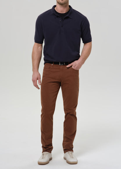 Person wearing brown straight leg pants with a navy crewneck short sleeve tee on a grey background.
