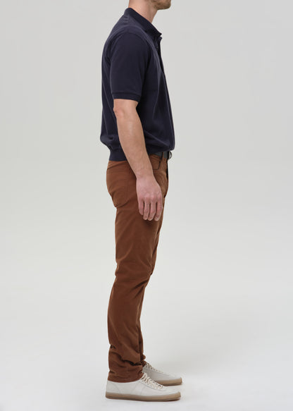 Person wearing brown straight leg pants with a navy crewneck short sleeve tee viewed from the side on a grey background.