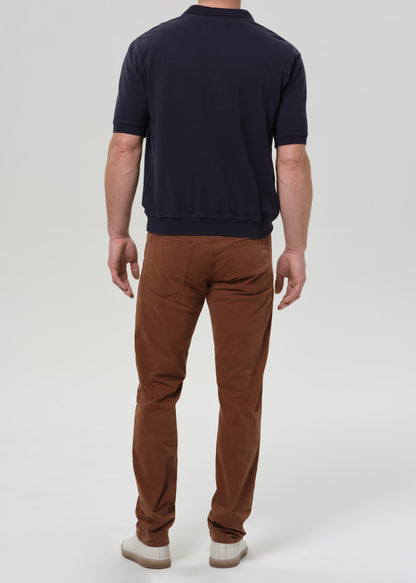 Person wearing brown straight leg pants with a navy crewneck short sleeve tee viewed from the back on a grey background.