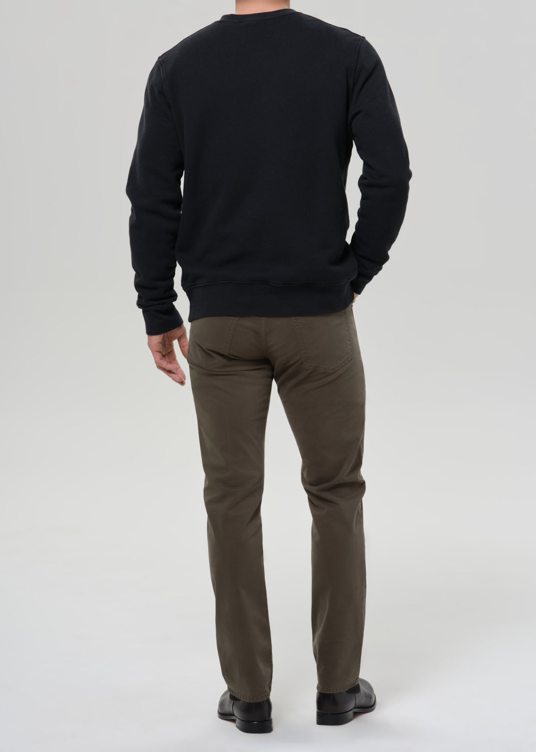 Man wearing a black sweatshirt and olive pants on a grey background