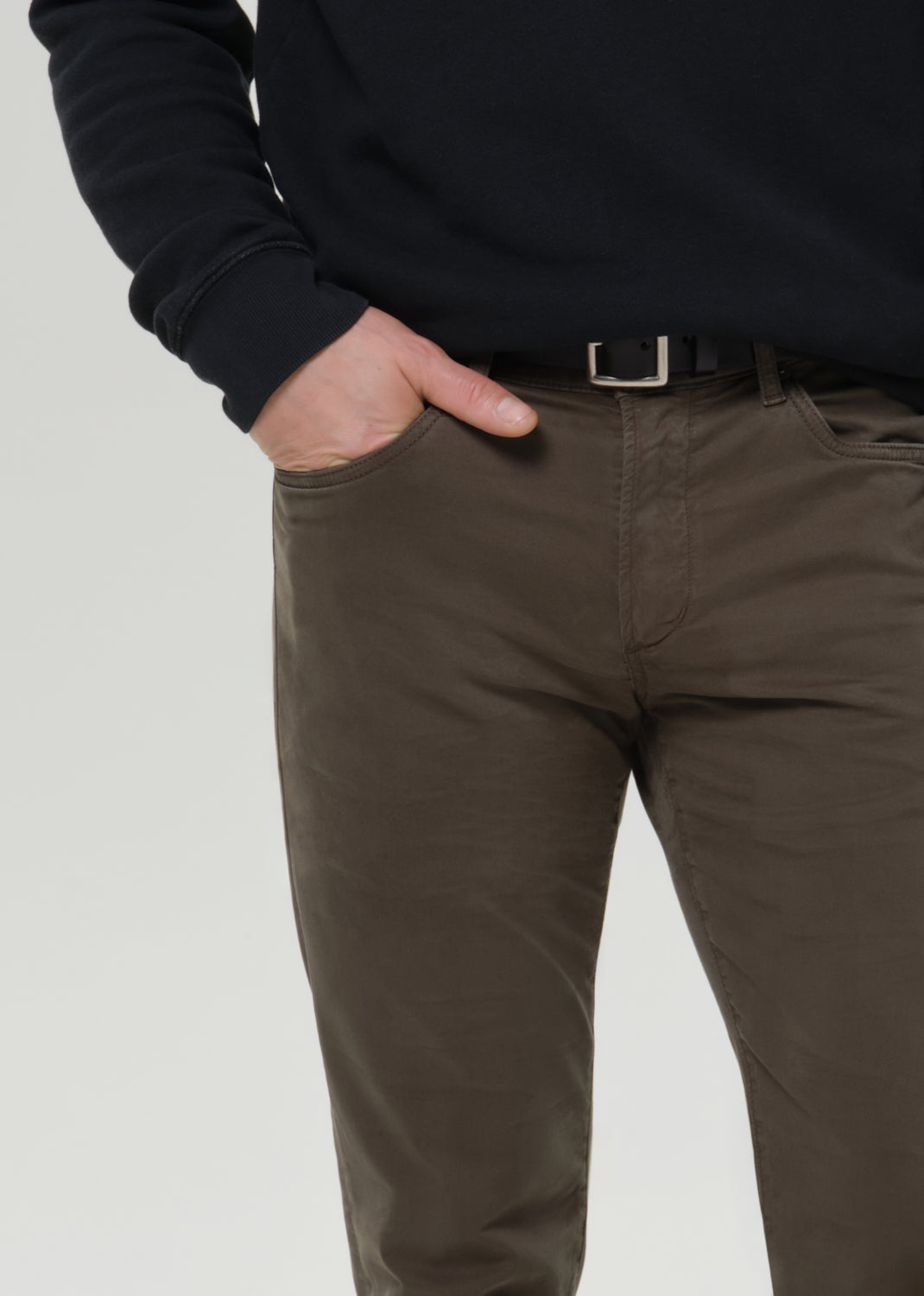 Man wearing a black sweatshirt and olive pants on a grey background