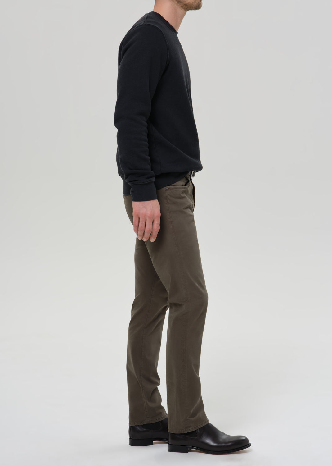 Man wearing a black sweatshirt and olive pants on a grey background