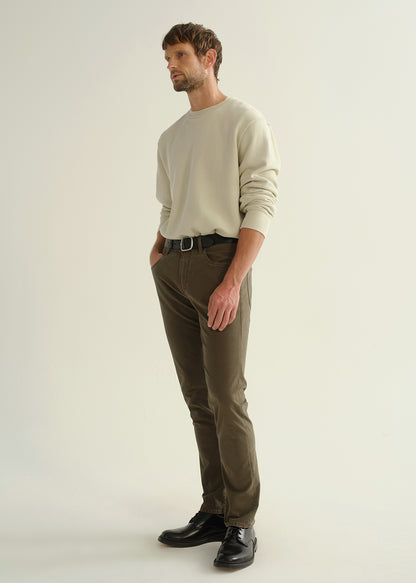 Person wearing a light grey crewneck sweatshirt, dark olive green pants, and black leather shoes, angled front full body view on a light grey background.