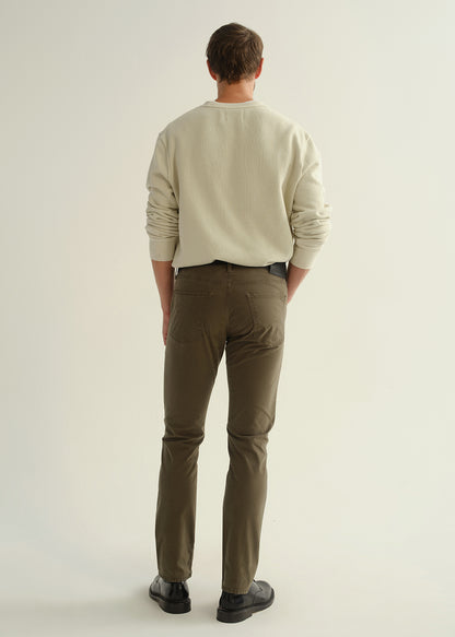Person wearing a light grey crewneck sweatshirt, dark olive green pants, and black leather shoes, back full body view on a light grey background.