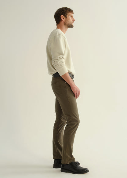 Person wearing a light grey crewneck sweatshirt, dark olive green pants, and black leather shoes, side full body view on a light grey background.