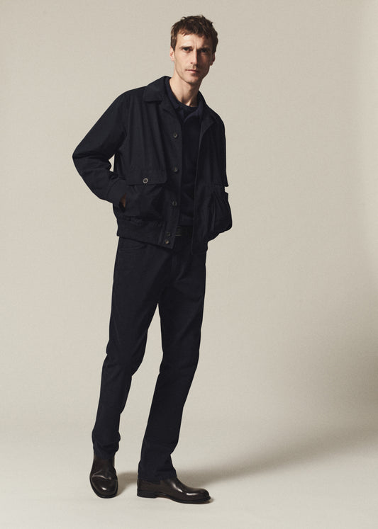 A man modeling a dark navy blue jacket and matching trousers against a plain beige studio background.