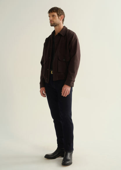 Person wearing a dark brown button-front jacket with flap pockets, dark indigo jeans, and black leather boots, front full body view on a light grey background.