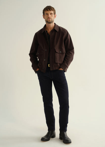 Person wearing a dark brown button-front jacket with flap pockets, dark indigo jeans, and black leather boots, angled front full body view on a light grey background.