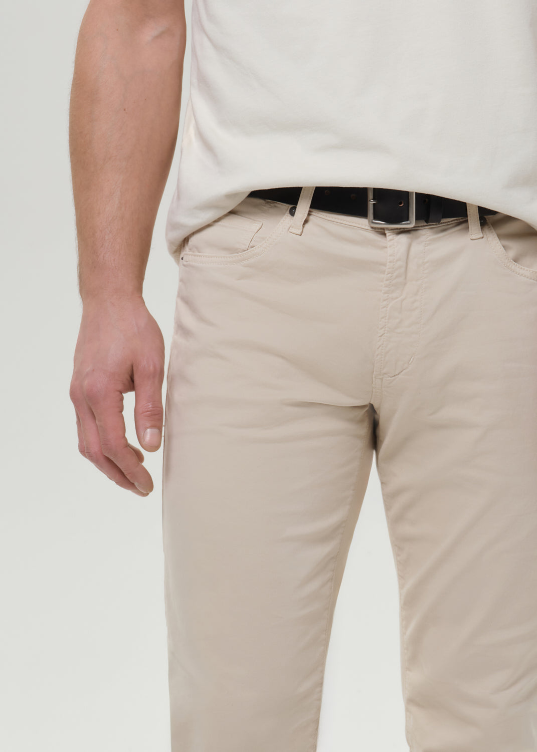 Close-up of cream straight leg pants on a grey background.
