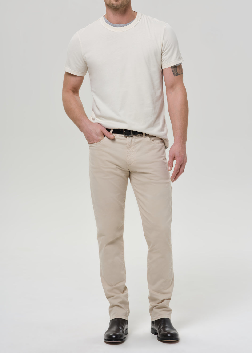 Person wearing cream straight leg pants with a white crewneck short sleeve tee on a grey background.
