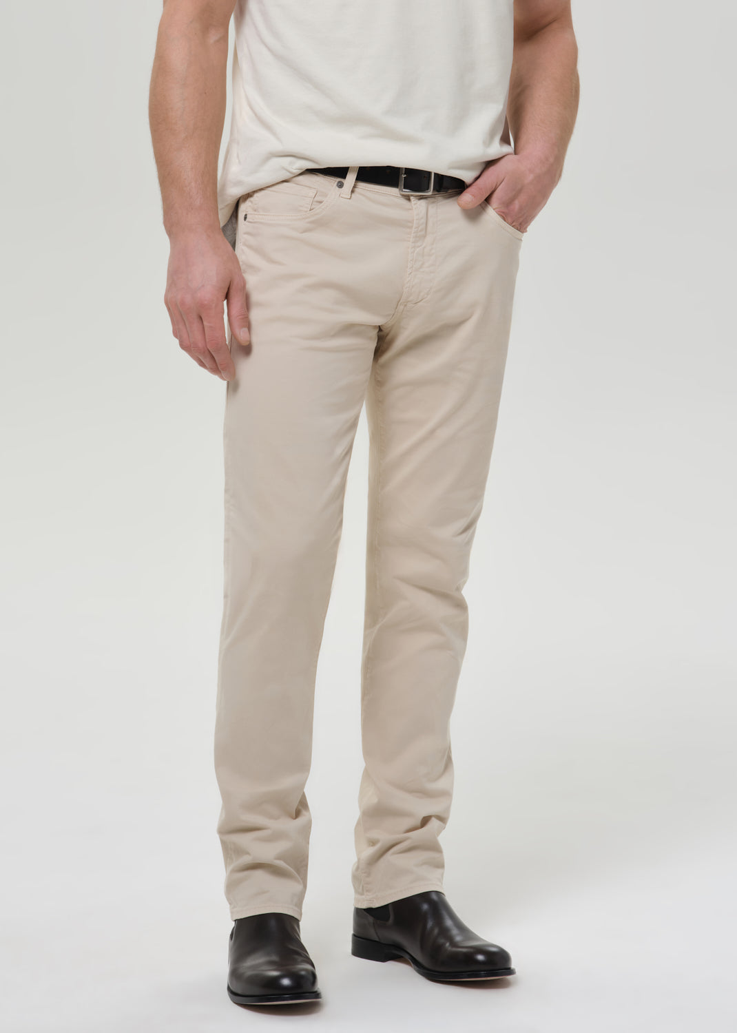 Person wearing cream straight leg pants with a white crewneck short sleeve tee on a grey background.