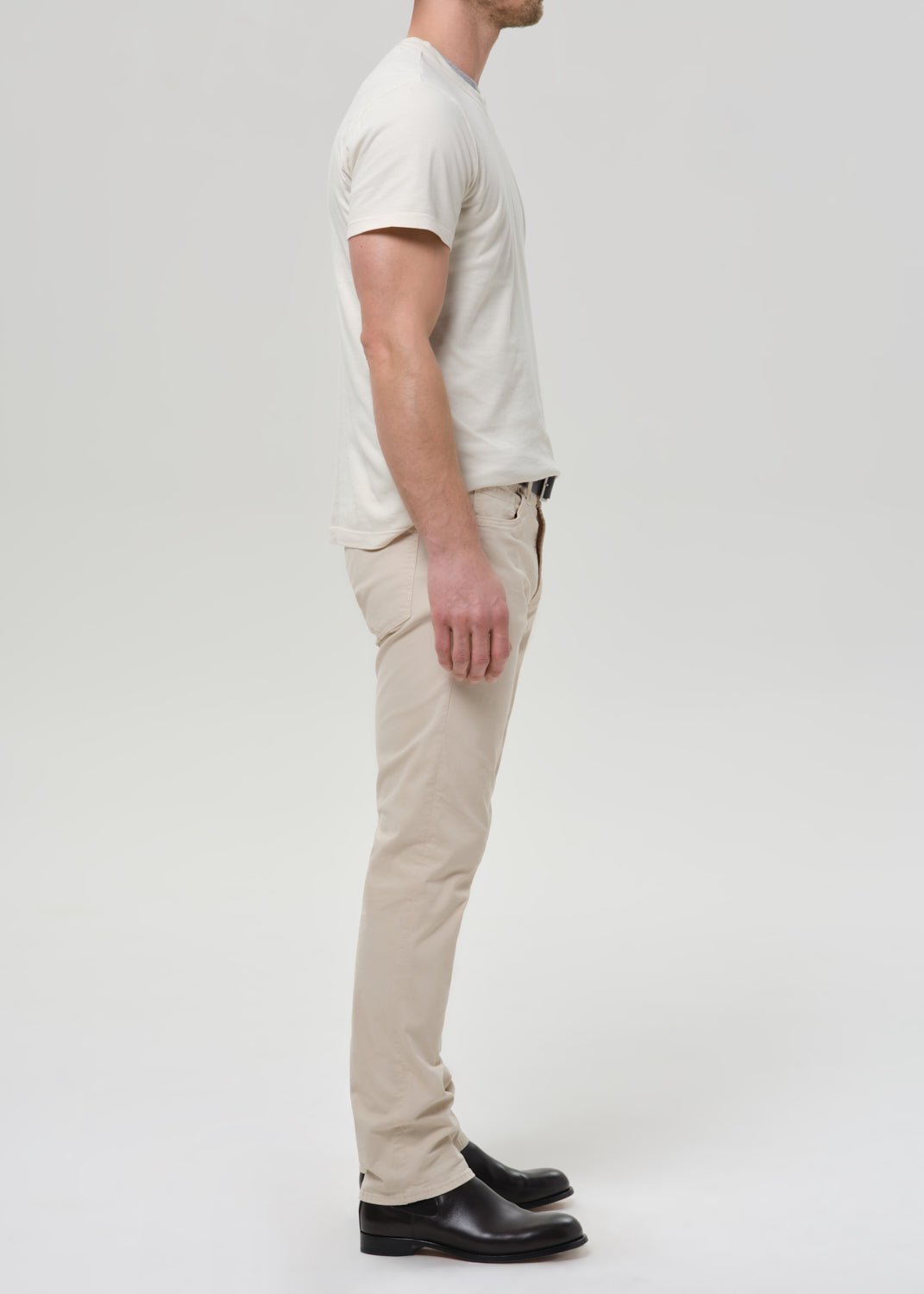 Person wearing cream straight leg pants with a white crewneck short sleeve tee viewed from the side on a grey background.
