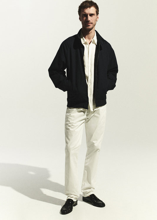 Man wearing a navy jacket, white shirt, and white pants on a white background