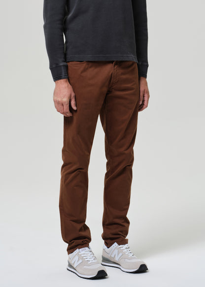 Person wearing a grey long-sleeve shirt and brown pants on a grey background